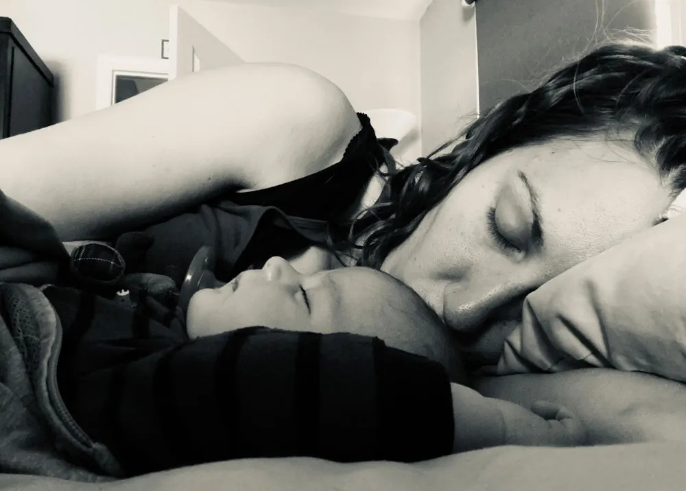 A black-and-white photo of a mother lying in bed nose-to-nose with her sleeping baby